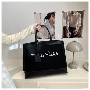 Detail of black canvas tote bag with Frida Kahlo script and leather handle trim