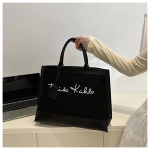 Detail of canvas tote bag with Frida Kahlo lettering and leather handles in office setting