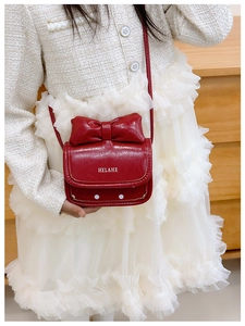Detalle de bolso para niña en cuero rojo brillante con lazo grande y logo HELAHE