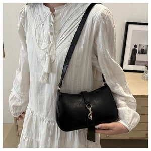 Close-up of black baguette bag with gold hook buckle on a white bohemian dress