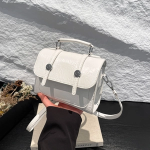 Détail de la texture en cuir plissé blanc sur un sac bandoulière avec boucles argentées