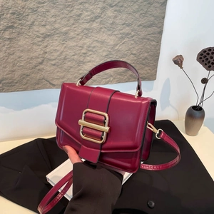 Burgundy matte leather crossbody bag with gold buckle and top handle held by hand