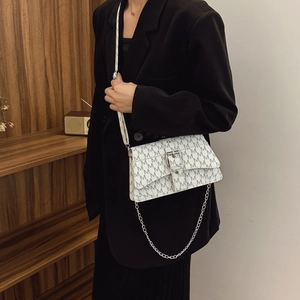White crossbody bag with black M pattern and silver chain on a black suit model