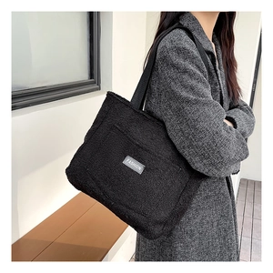 Dettaglio della borsa tote in peluche nera con etichetta FASHION su cappotto grigio