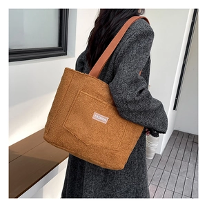 Dettaglio borsa tote in peluche marrone con tasca esterna ed etichetta tessuta 'FASHION'