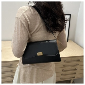 Detail of a black leather underarm bag with a golden rectangular buckle on the flap