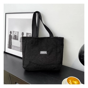 Dettaglio ravvicinato della borsa tote in pile nero con etichetta moda minimale