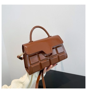 Detail of chocolate brown textured crossbody bag with square embossed pattern and gold hardware