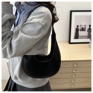 Detail of minimalist black leather hobo bag with smooth curved silhouette and shoulder strap