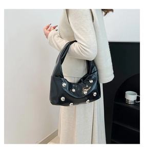 Chic black crescent underarm bag with silver studs worn by a model in a minimal setting