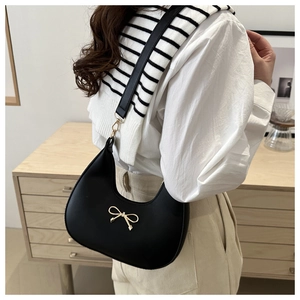 Close-up of black hobo shoulder bag with elegant gold bow detail on a model
