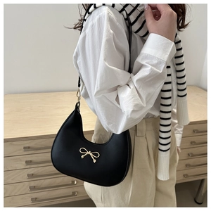Detail of a black underarm hobo bag featuring a gold bow emblem and slim shoulder strap