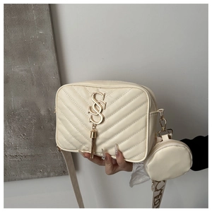 Detail of beige quilted crossbody bag featuring golden S logo and a round coin purse charm