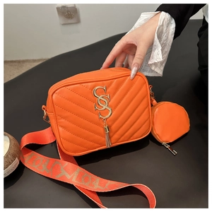 Detail of orange quilted crossbody bag with gold logo, fringe charm and round coin purse