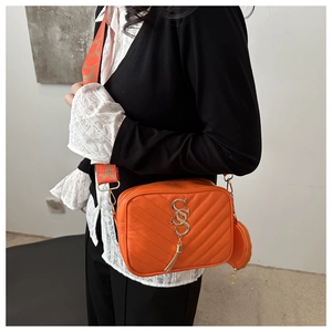 Detail of orange quilted crossbody bag featuring gold metal fringe and a round coin purse