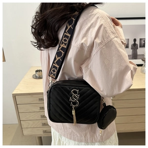 Close-up of black quilted crossbody bag with metal tassel and printed wide strap