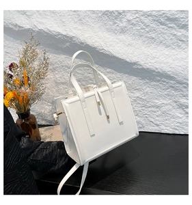 Detail of white leather shoulder bag with gold hardware and decorative tassel on table