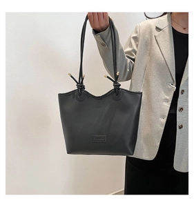 Close-up of black tote bag featuring unique knot handles and gold metal accents