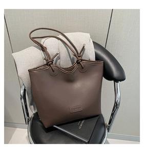 Detail of deep brown tote bag featuring knotted shoulder straps and embossed fashion tag