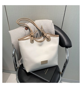 Close-up of cream tote bag with fashion tag and brown leather handles on a chair