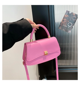 Dettaglio di borsa quadrata rosa acceso con chiusura dorata e manico in pelle chic