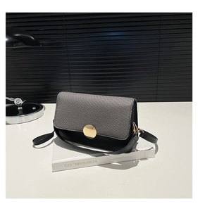 Detail of the chic black and grey contrast crossbody bag with a round gold buckle on a book
