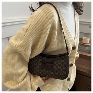 Detail of dark brown baguette bag with letter print and leather bow on shoulder strap