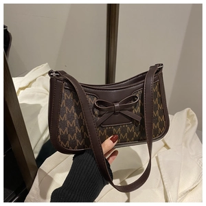 Detail of a dark brown shoulder bag with monogram print and a bow decoration