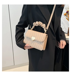 Dettaglio di una borsa crema chic con trama a pieghe e chiusura a cuore dorato