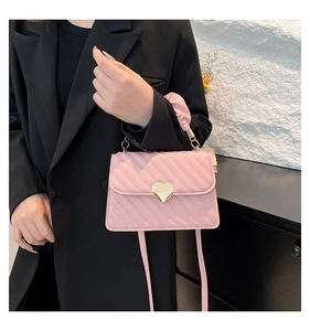 Detail of pink quilted handbag with gold heart buckle and ruched handle worn by model