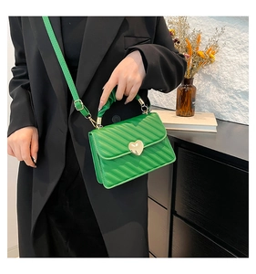 Dettaglio della borsa verde trapuntata con fibbia a cuore dorata su un blazer nero
