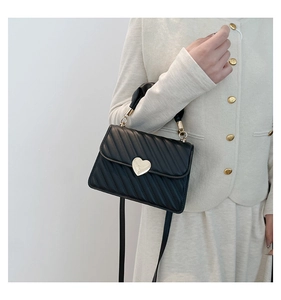 Detail of black quilted shoulder bag featuring gold heart lock and pleated silk scarf handle