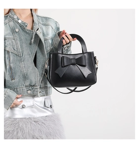 Detail of elegant black square handbag featuring a large decorative bow and top handle