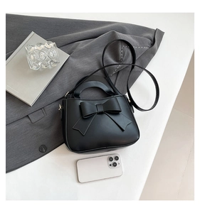 Close-up of black bow handbag with crossbody strap and smartphone for scale reference
