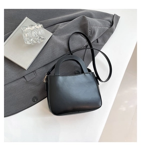 Close-up of matte black leather handbag showing golden metal buckle and minimalist handle