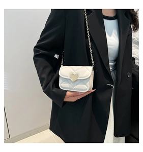Gros plan du mini sac blanc matelassé avec fermoir cœur doré sur un blazer noir