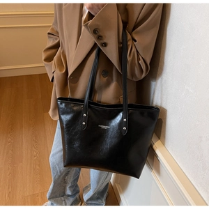 Detail of black faux leather tote bag with FASHION & BAGS branding and rivet reinforcement