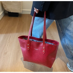 Detailed close-up of a red vintage leather tote bag with fashion lettering and rivets