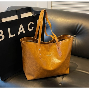 Detail view of large brown vintage tote bag with rivets and text on a leather sofa