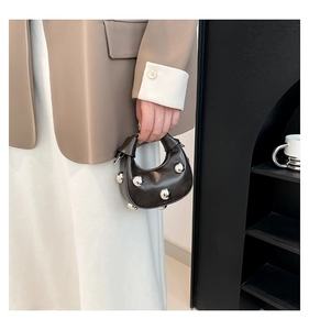 Close-up of a brown leather crescent handbag with large silver studs held by a model