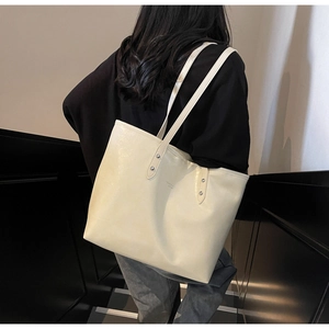 Detail shot of a large off-white tote bag carried by a model in a minimalist setting