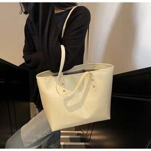 Detail view of cream white leather tote bag featuring silver rivet studs and slim straps
