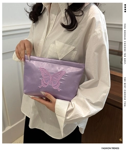 Detail of purple satin clutch with butterfly embroidery held by a model in white