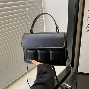 Detail of a black structured chocolate block handbag with metallic hardware and sleek strap