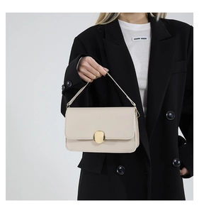 Détail d'un sac à main beige minimaliste avec boucle ronde dorée et texture lisse de cuir