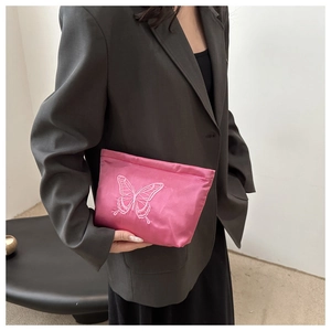 Detail of vibrant pink satin clutch with elegant butterfly embroidery held by a model