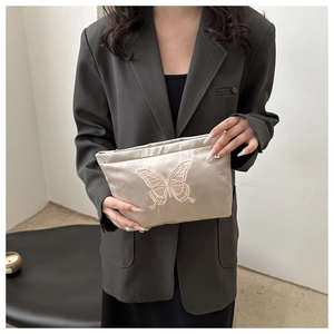 Detail of elegant champagne satin clutch bag with butterfly embroidery held by model