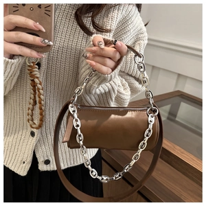 Close-up of brown cylindrical crossbody bag with silver chain strap and leather detail