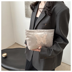 Champagne gold satin bag with butterfly embroidery held by a model in a minimal setting