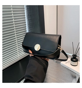 Close-up of black leather crossbody bag featuring a round silver buckle and detachable strap